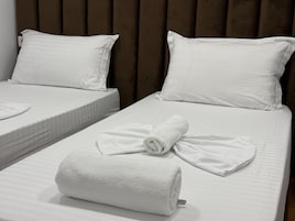 Dos camas individuales con sábanas y almohadas blancas, una toalla blanca enrollada sobre la cama y un cabecero de madera.