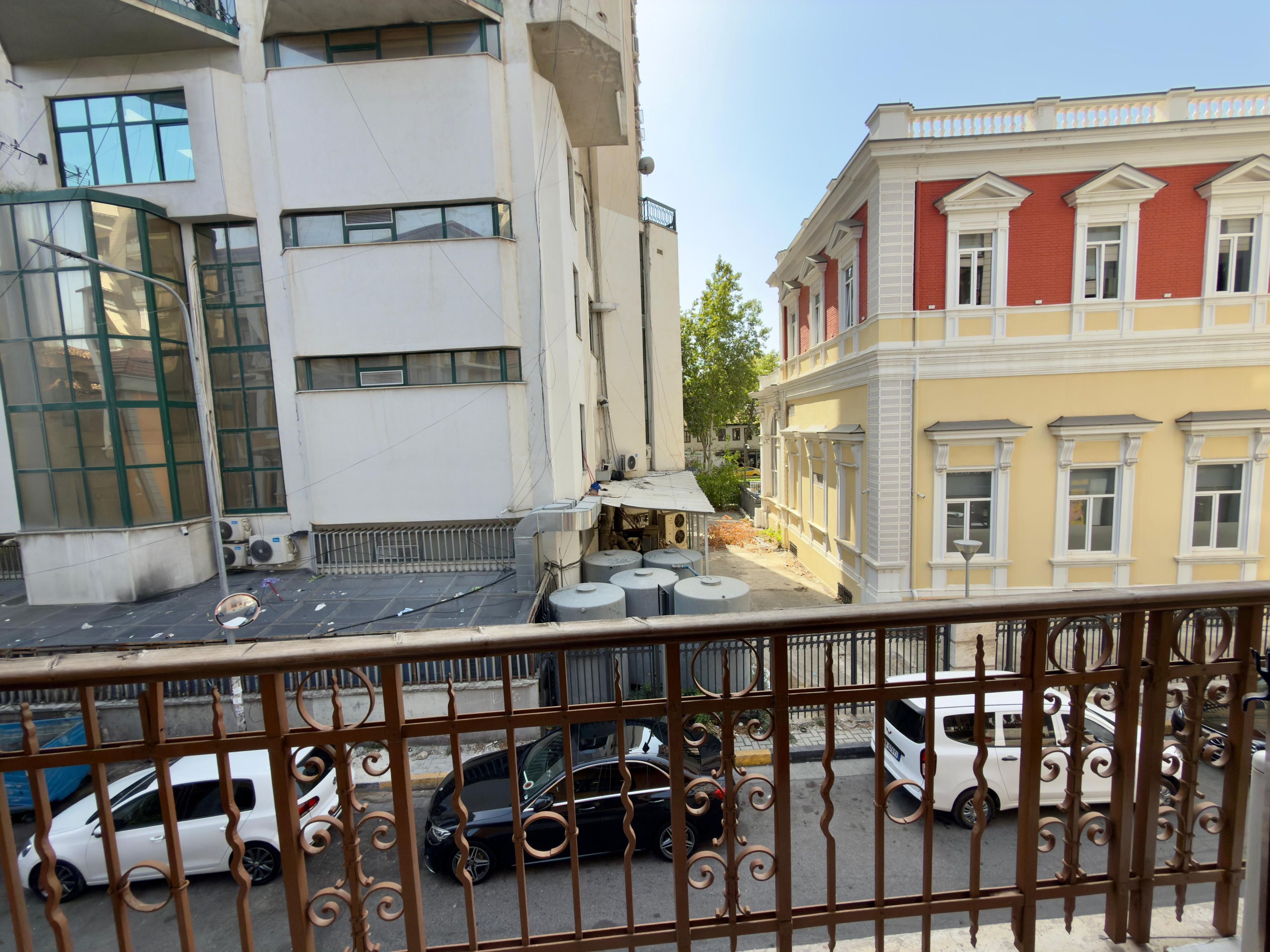 Una vista di strada con edifici, auto parcheggiate e un cancello in metallo.
