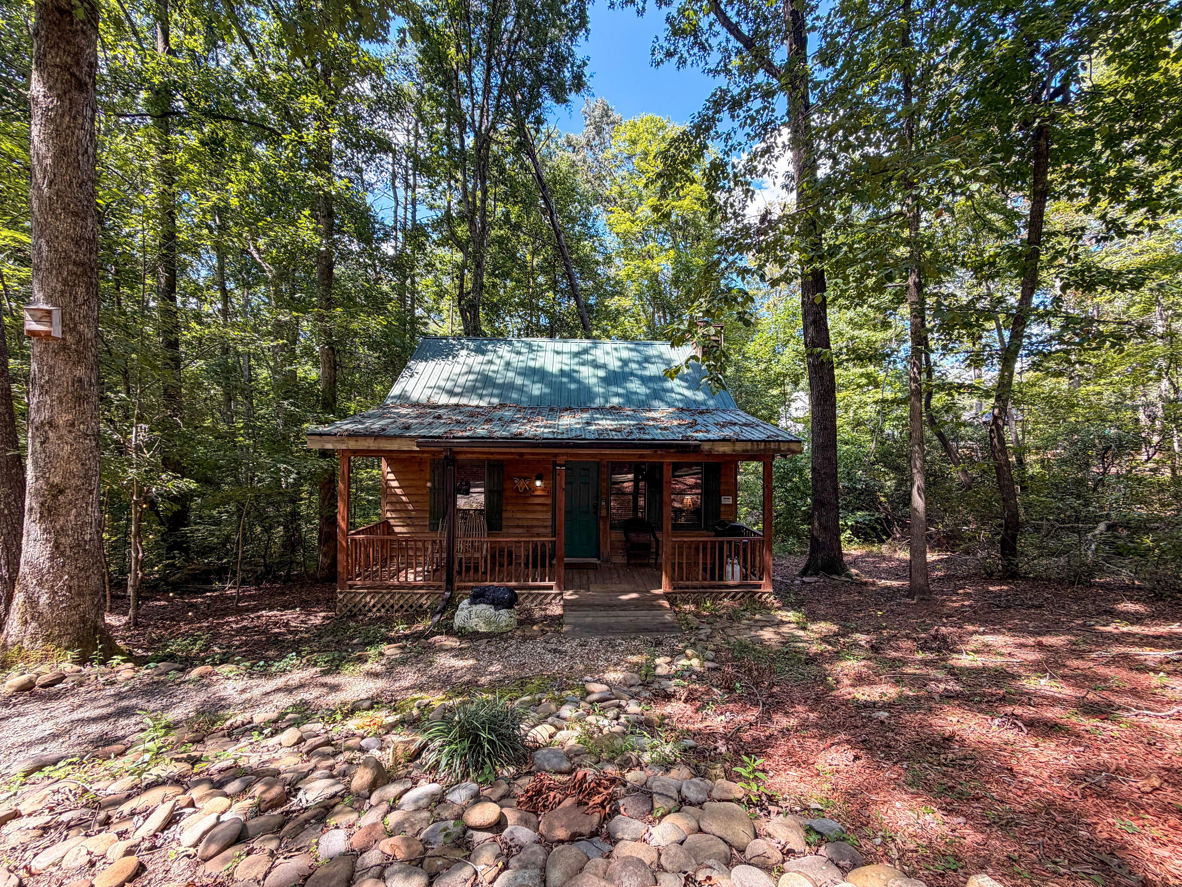 A rustic cabin with a porch, surrounded by a forest.