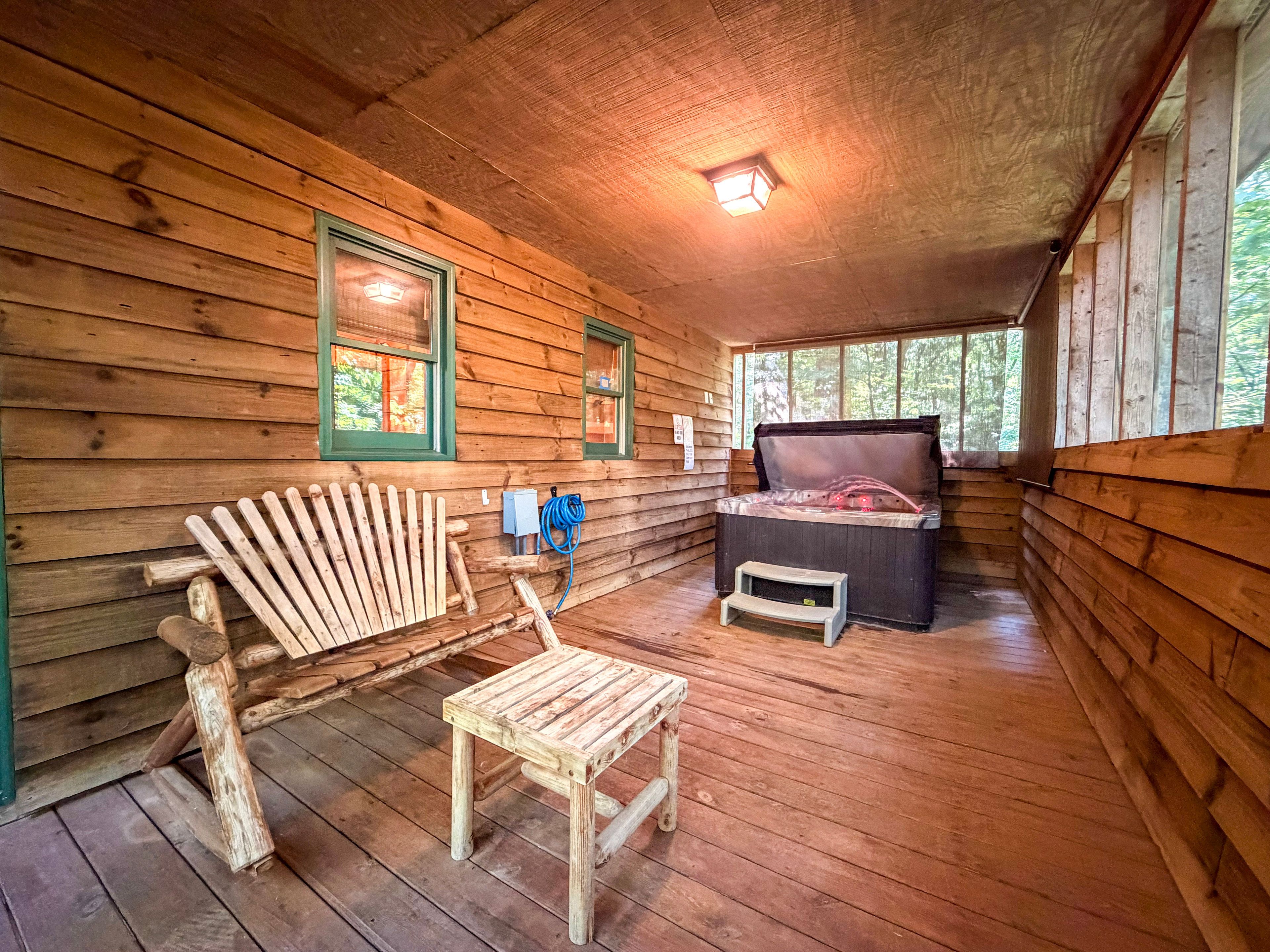 A cabin interior with a wooden floor, a bed with a headboard, a wooden chair, and a small table.