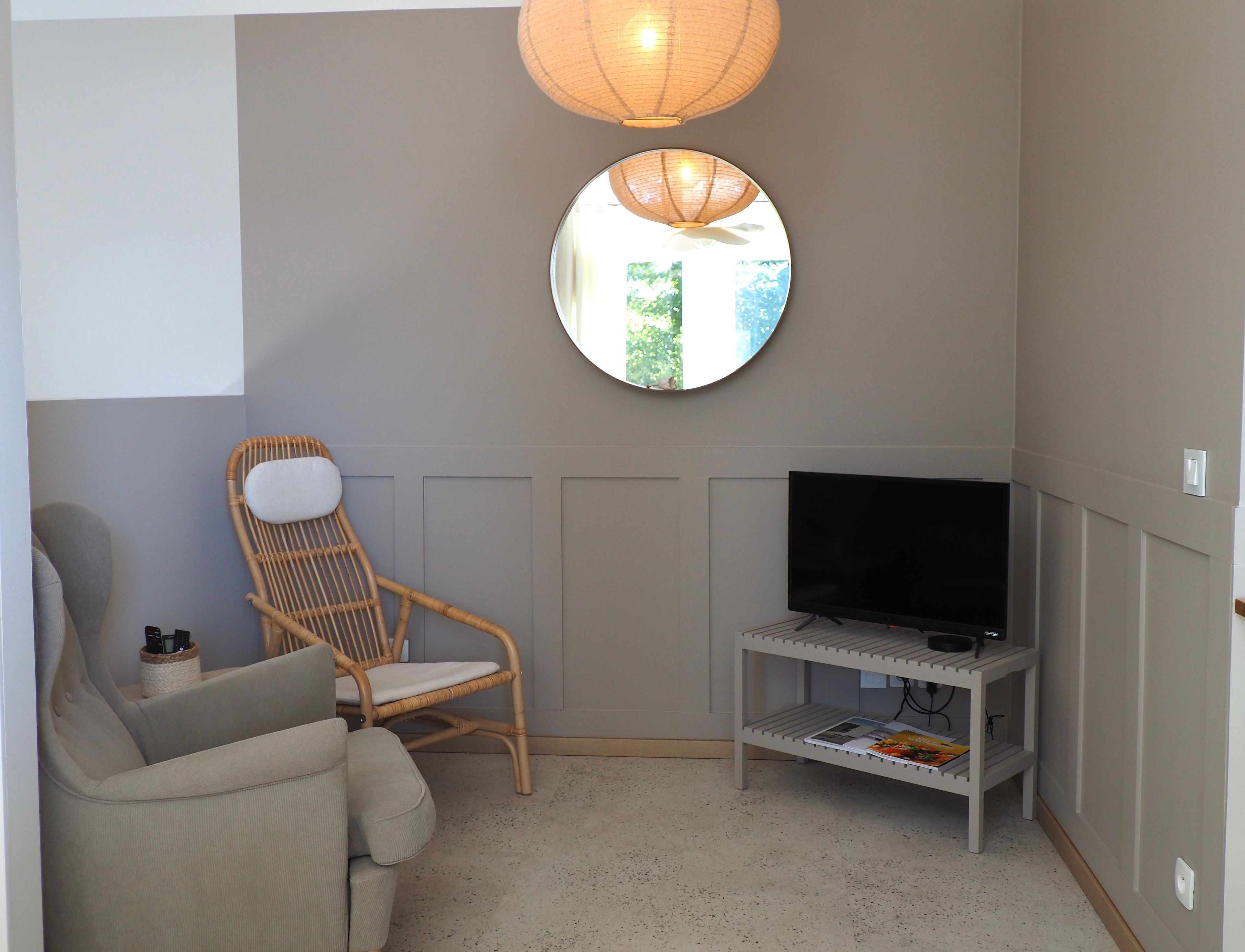 Een kamer met een televisie op een standaard, een rieten stoel, een bank en een spiegel aan de muur.