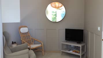 Een kamer met een televisie op een standaard, een rieten stoel, een bank en een spiegel aan de muur.