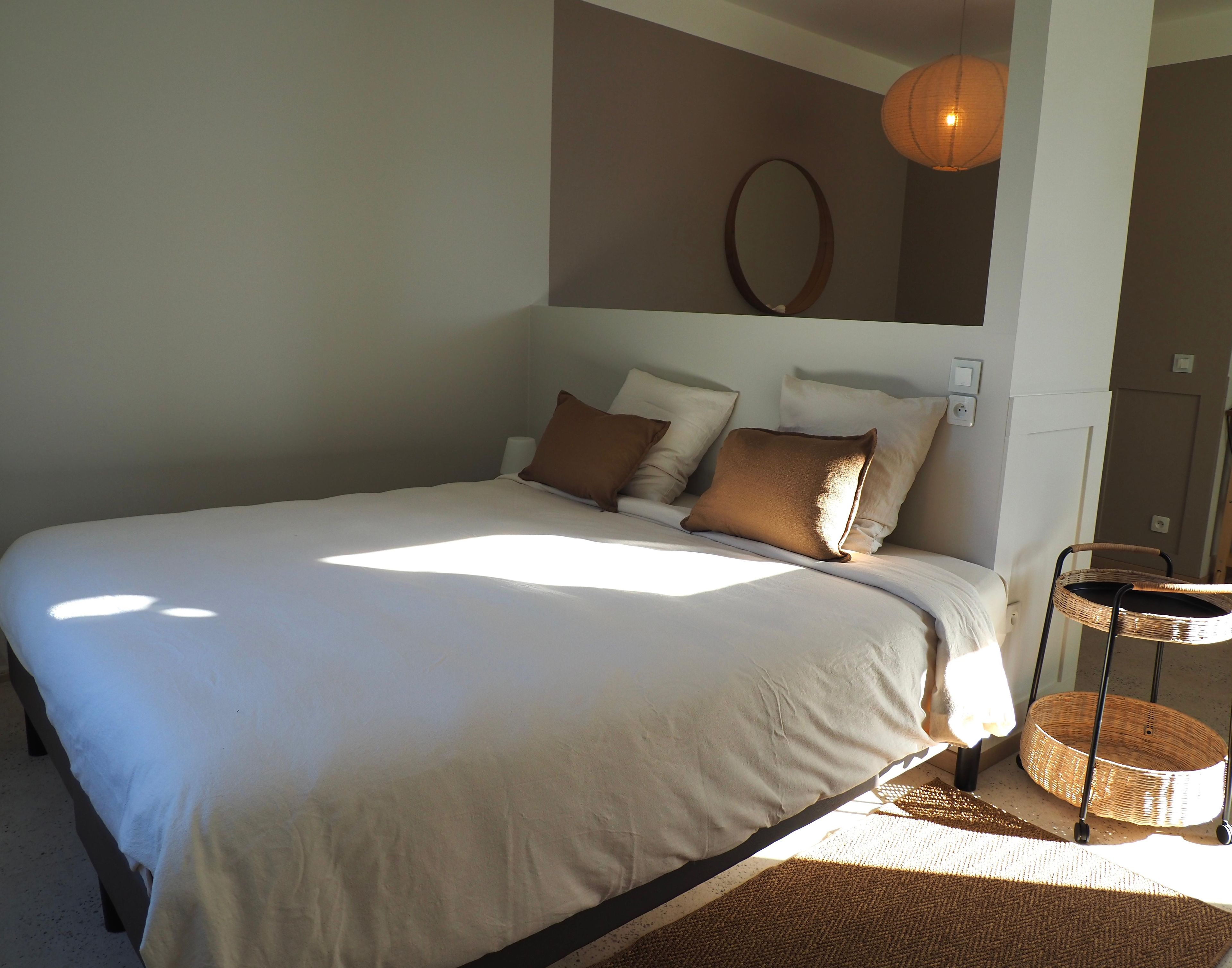 Une chambre à coucher avec un grand lit, une table de chevet, un miroir fixé au mur et un luminaire suspendu.