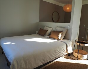 A bedroom with a large bed, a bedside table, a wall-mounted mirror, and a hanging light fixture.