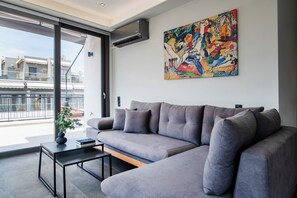 A modern living room with a grey sofa, a coffee table, and a colorful abstract painting on the wall. - Chic Penthouse with Panoramic Wrap-Around City Views (Athina)