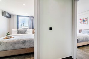 A modern hotel room with a bed, a bedside table with a cup and saucer, and a window with curtains. - Chic Penthouse with Panoramic Wrap-Around City Views (Athina)