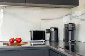 Et køkken med et moderne design, med en Bosch kaffemaskine, en De'Longhi espressomaskine og en Braun brødrister.