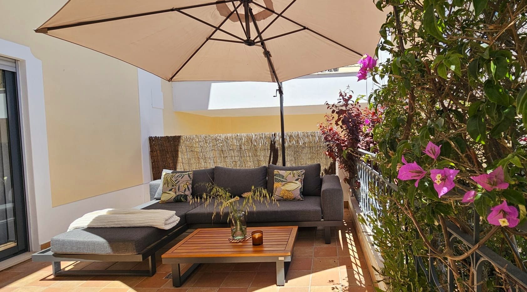 A balcony with a sofa, a table, and a large umbrella.