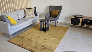 Ein Wohnzimmer mit grauem Sofa, einem kleinen runden Tisch, einem grauen Sessel und einem Holztischchen mit einer Schüssel.