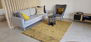Ein Wohnzimmer mit grauem Sofa, einem kleinen runden Tisch, einem grauen Sessel und einem Holztischchen mit einer Schüssel.