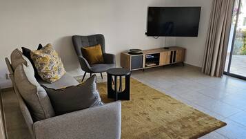 A living room with a sofa, armchair, and a TV on a stand.