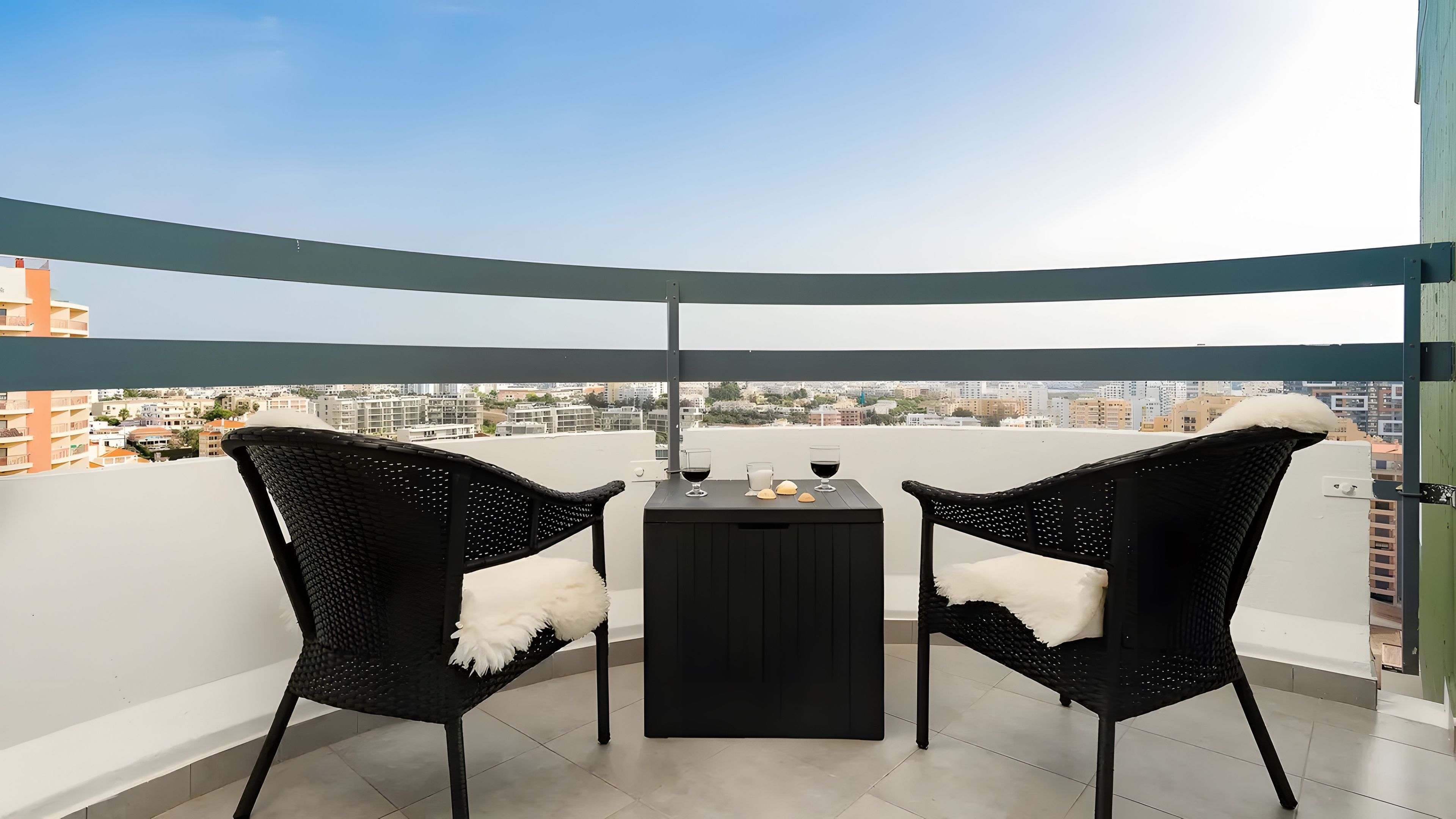 Een balkon met twee stoelen, een tafeltje en uitzicht op de stad.