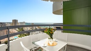 A balcony with a table, chairs, a vase with flowers, and a view of the sea and buildings. - Apartment 'Vista Bonita' with Sea View, Wi-Fi and Air Conditioning (Portimão)