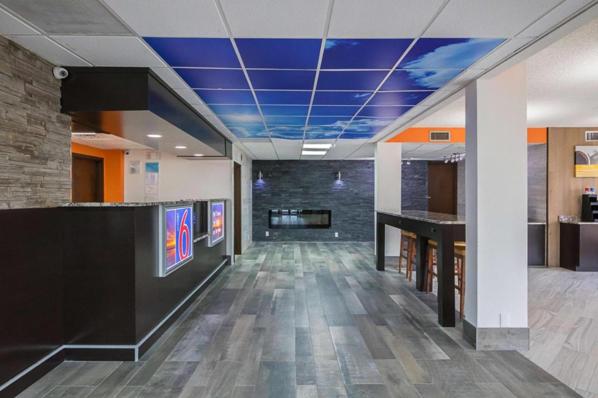 A reception area with a modern design, including a reception desk, a wall-mounted TV, and a ceiling with a blue sky pattern.