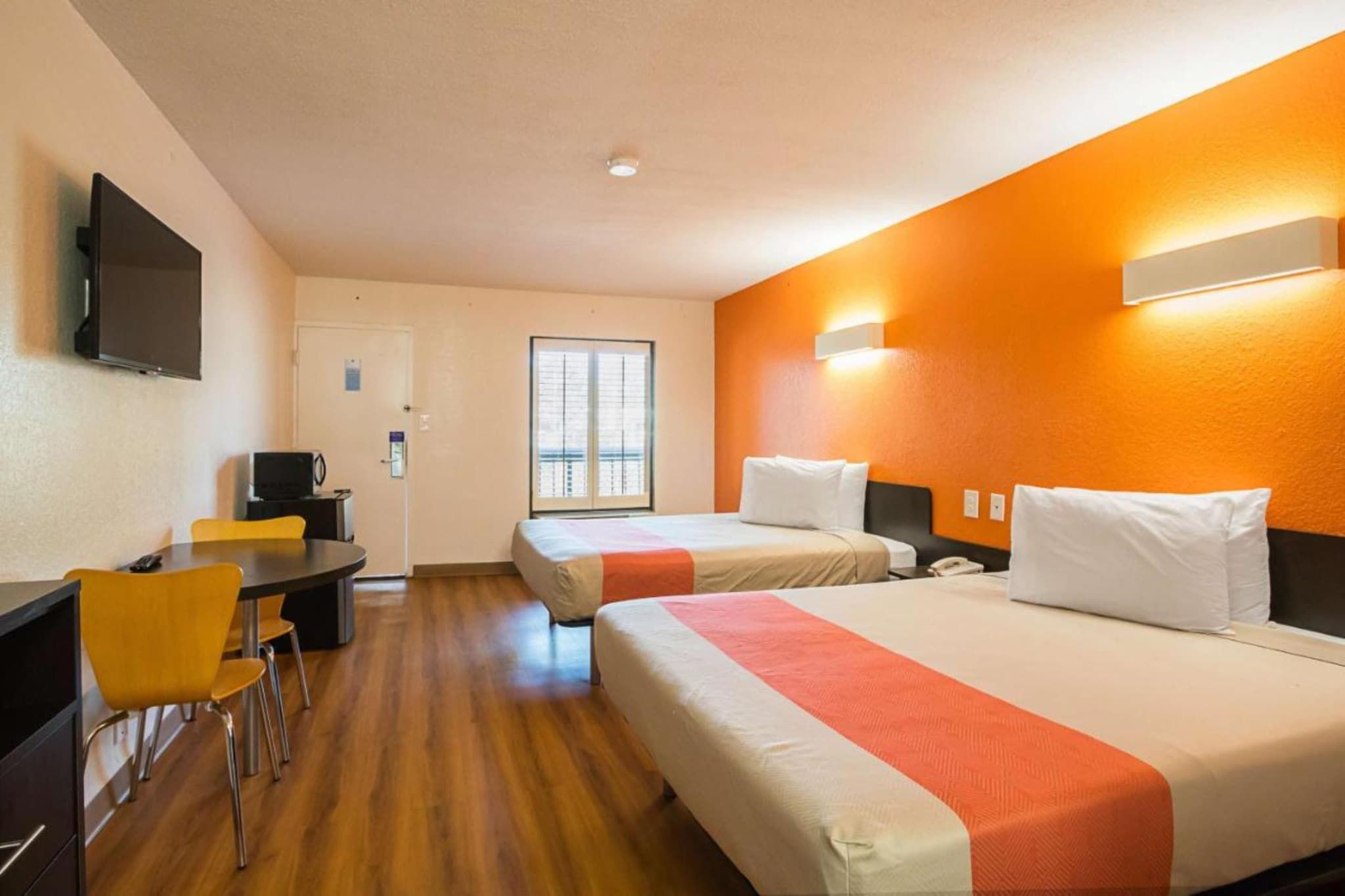 A hotel room with two beds, a desk, a chair, a television, and a window.