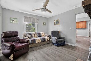 A living room with a ceiling fan, a leather armchair, a sofa with a patterned blanket, a quilted chair, and a window with blinds. - Cozy Mount Airy Retreat | Wooded Yard Near Maybery (Mount Airy)