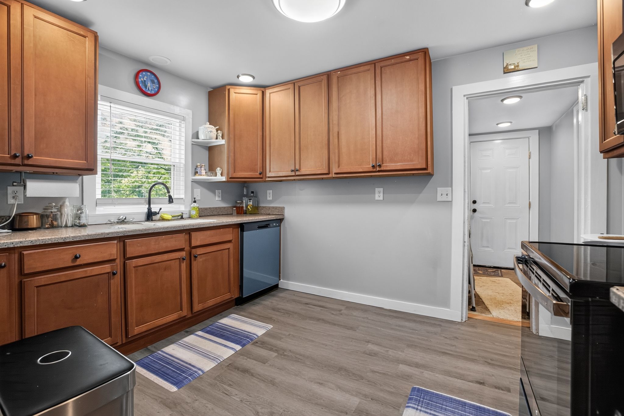 A kitchen with wooden cabinets, a dishwasher, a sink, and a window with blinds.