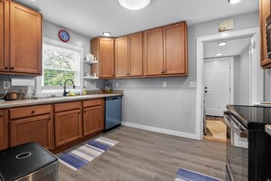 A kitchen with wooden cabinets, a dishwasher, a sink, and a window with blinds. - Cozy Mount Airy Retreat | Wooded Yard Near Maybery (Mount Airy)