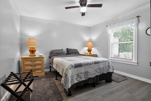A bedroom with a bed, two bedside tables with lamps, a ceiling fan, a window with blinds, and a chair. - Cozy Mount Airy Retreat | Wooded Yard Near Maybery (Mount Airy)