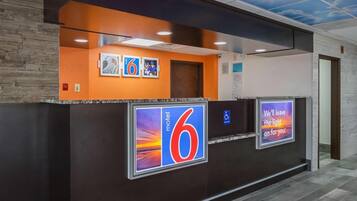 Zona de recepción de un hotel con un llamativo letrero con el número '6', un símbolo de accesibilidad para sillas de ruedas y una pantalla digital mostrando un mensaje.
