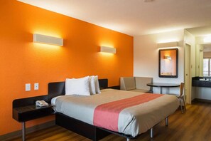 Een hotelkamer met een bed, nachtkastje, stoel en een klein bureau met een stoel.
