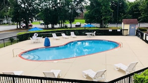 A swimming pool with lounge chairs and umbrellas, surrounded by a fence and trees. - 2 Queen Beds | Premium, Micfridge (Savannah GA)