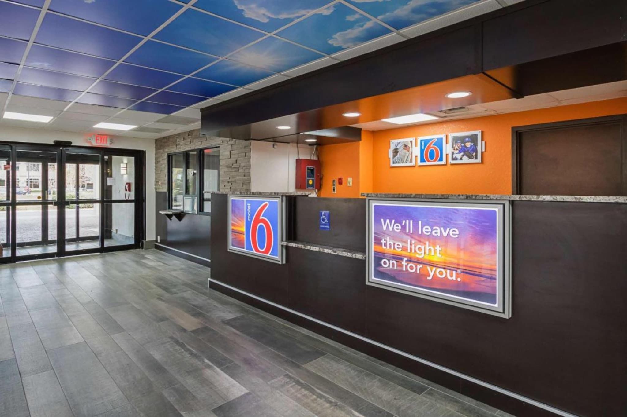 Zona de recepción de un hotel con un cartel digital que muestra el número 6, un símbolo de accesibilidad para sillas de ruedas y un cartel motivacional.