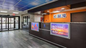 Zona de recepción de un hotel con un cartel digital que muestra el número 6, un símbolo de accesibilidad para sillas de ruedas y un cartel motivacional.