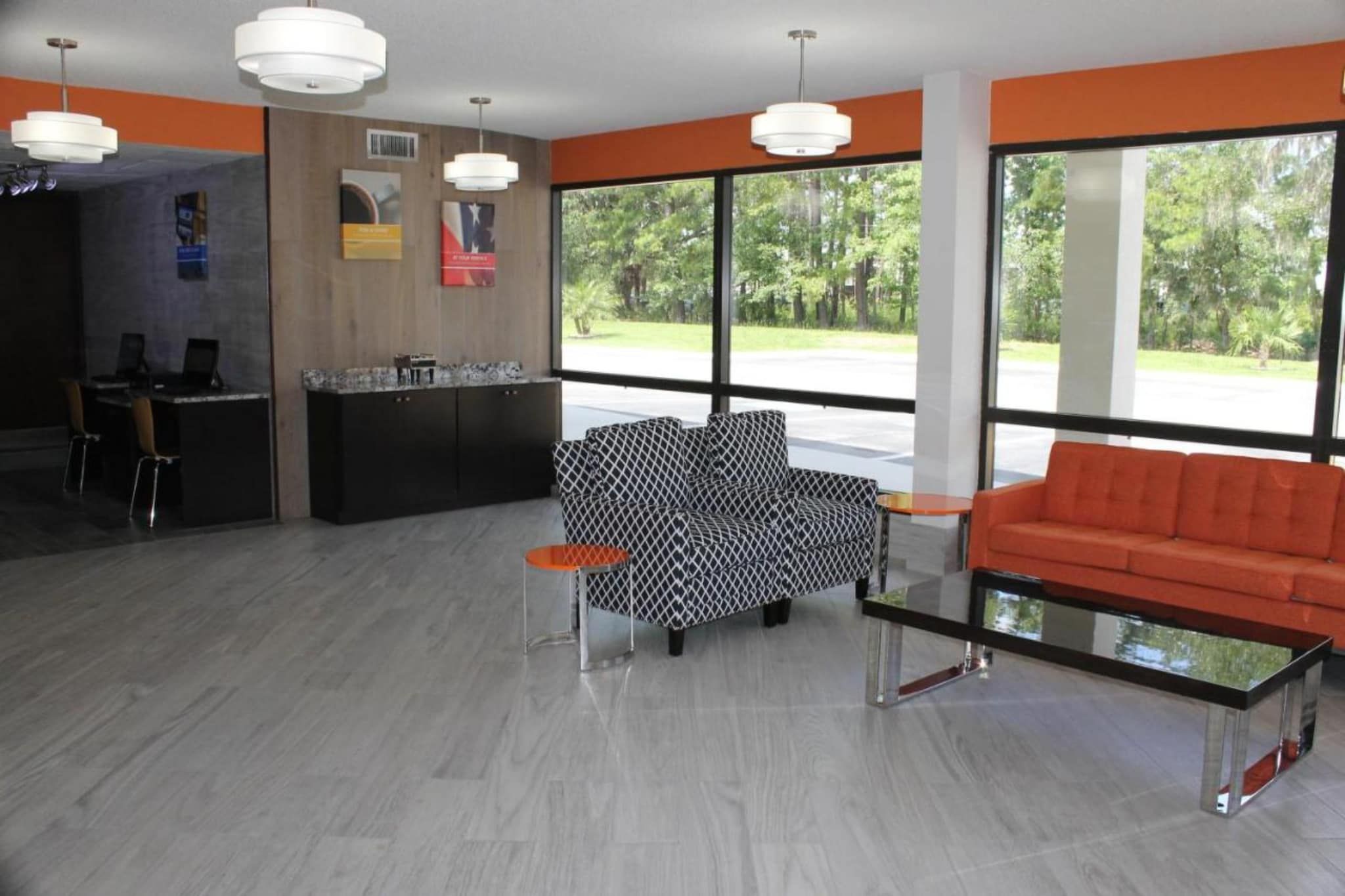 A modern lobby with a reception desk, a black and white patterned sofa, an orange couch, and large windows offering a view of greenery.