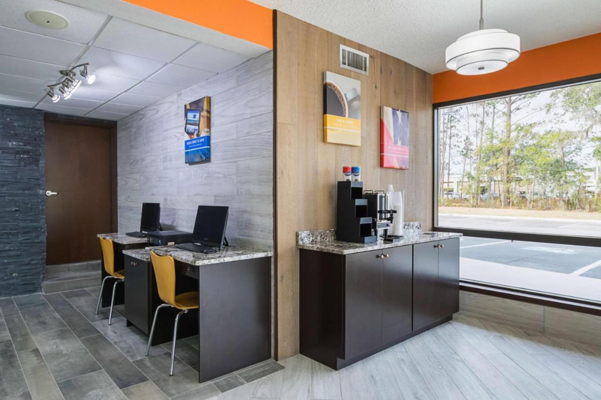 A reception area with a counter, two computers, a coffee machine, and a window with a view of trees.