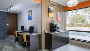 A reception area with a counter, two computers, a coffee machine, and a window with a view of trees.