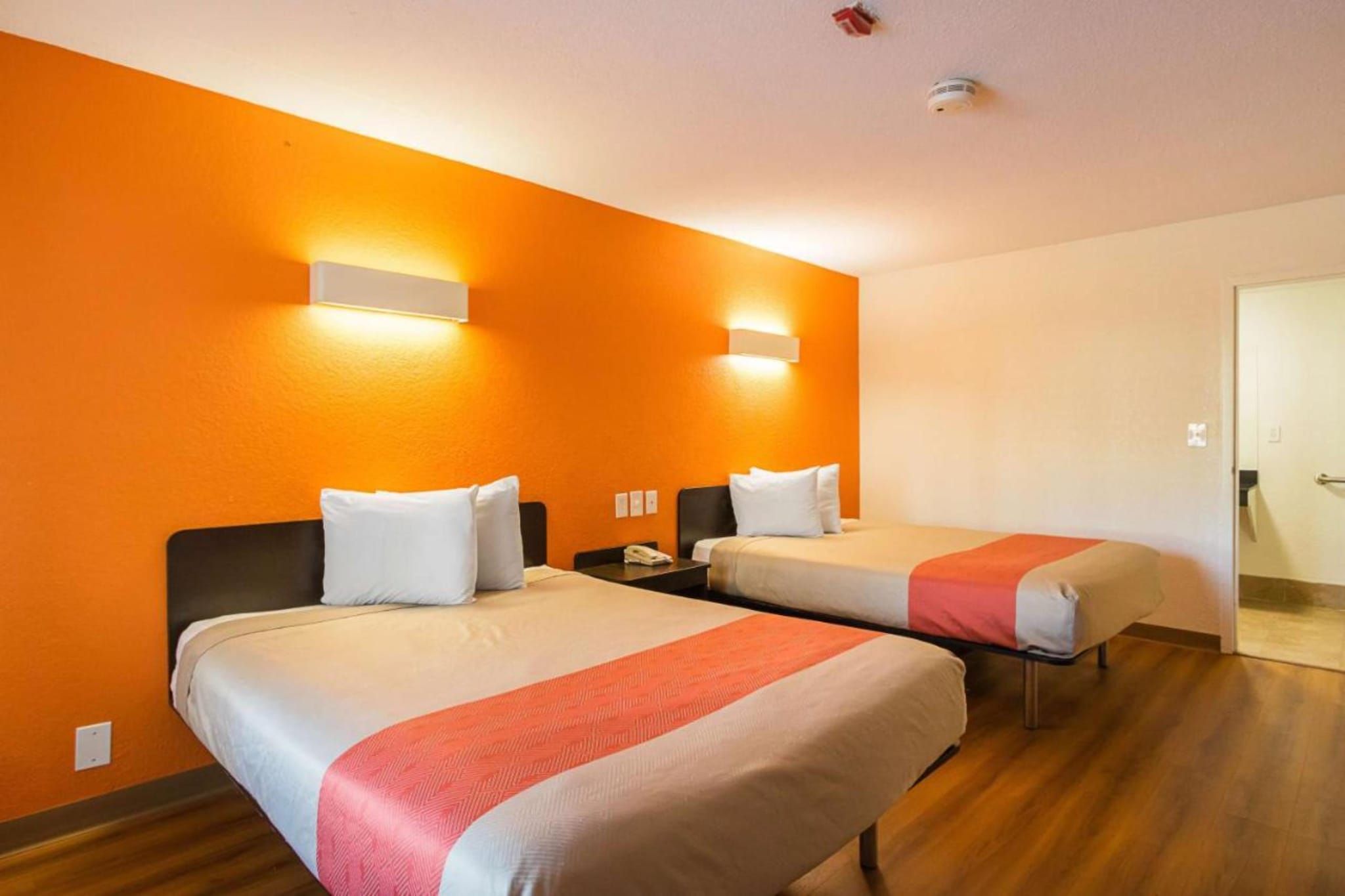 Habitación de hotel con dos camas, cada una con cabecero blanco y almohadas, y un detalle rojo en la colcha.