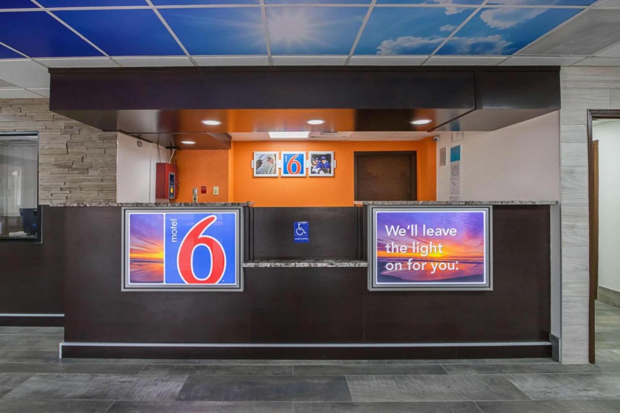 Mostrador de recepción de hotel con un cartel grande con el número 6, un letrero de acceso para discapacitados y una cita motivacional.