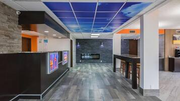 A reception area with a modern design, including a reception desk, a wall-mounted TV, and a ceiling with a blue sky pattern.
