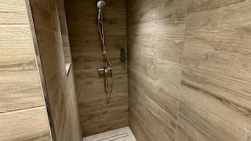 Un espace douche étroit aux murs recouverts de panneaux en bois, doté d’un pommeau de douche et d’un flexible de douche.