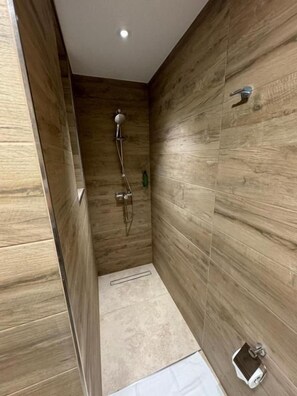 A narrow shower area with wooden panel walls, a showerhead, and a handheld shower attachment.