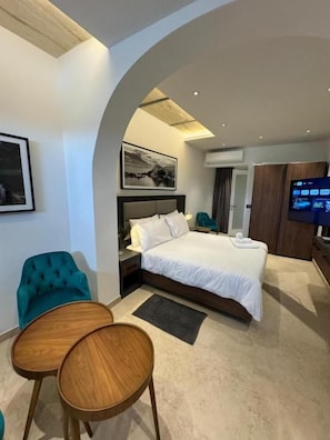 A modern hotel room with a curved ceiling, a large bed, a television, and a seating area with two wooden chairs. - Marea Seafront (Kalkara)
