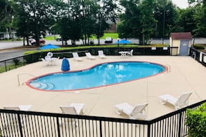 Una piscina con sillas de descanso y sombrillas, rodeada por una cerca y árboles.