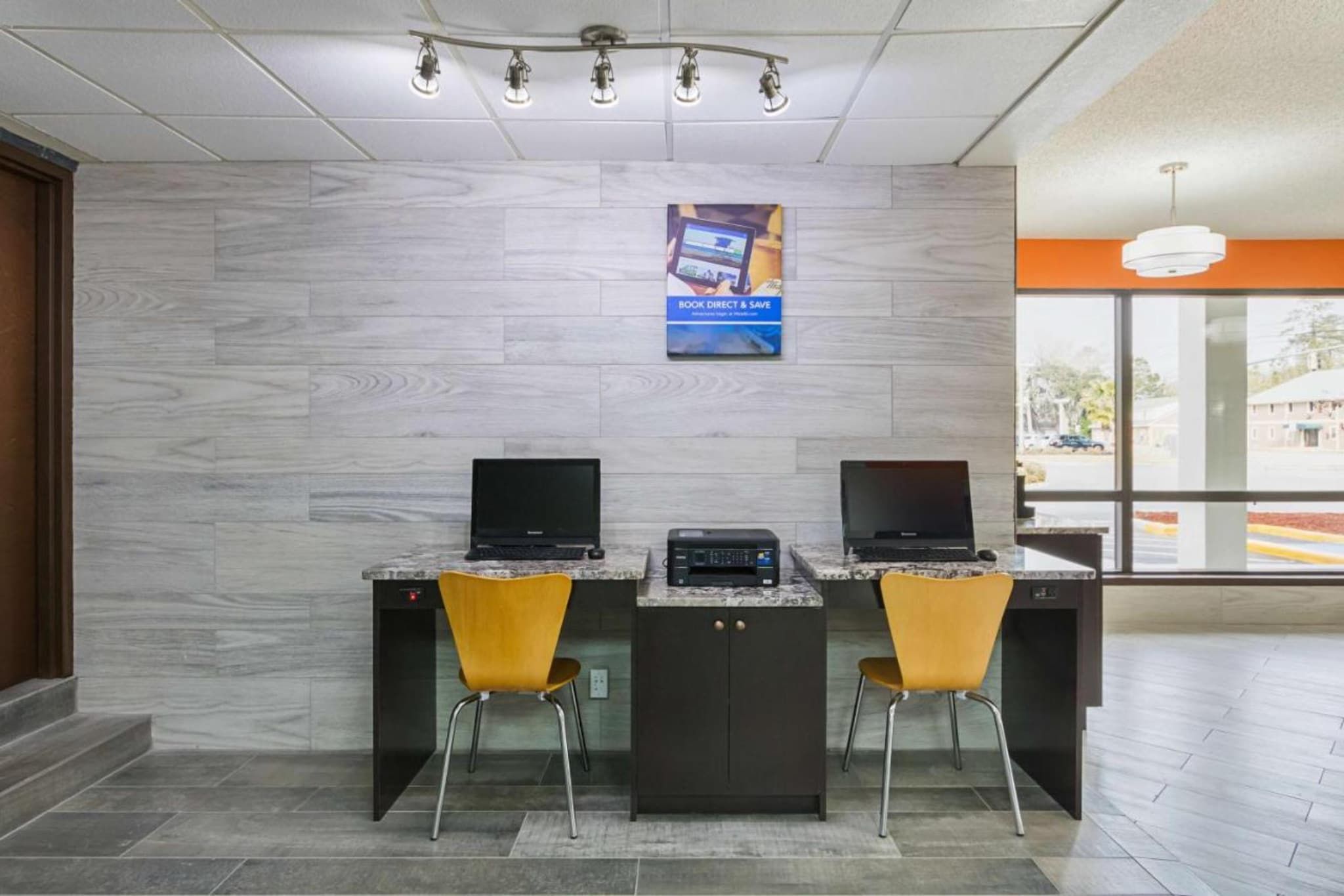 A reception area with two desks, each with a computer and a chair. There is a poster on the wall above the desks.