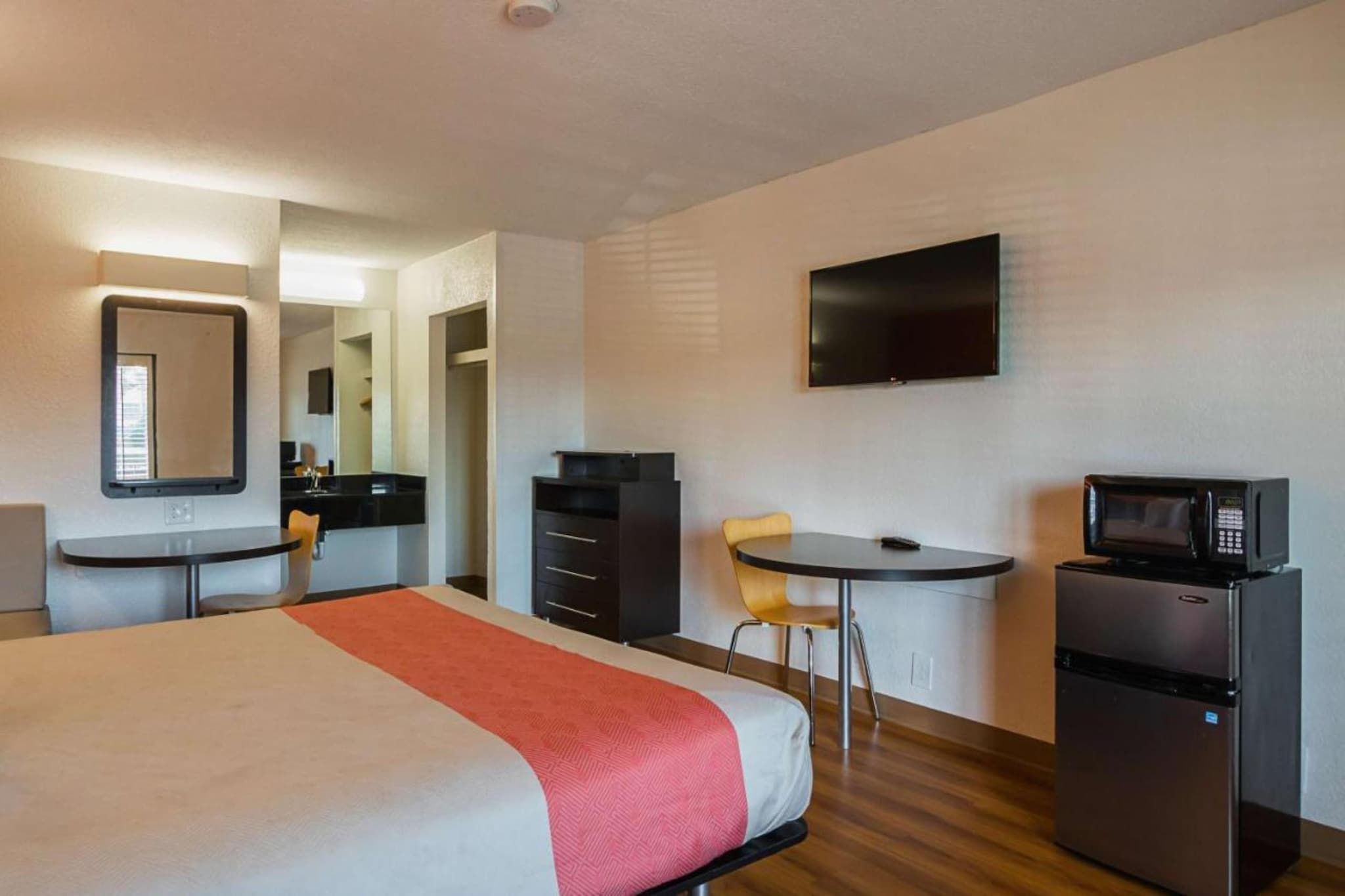 Habitación de hotel con cama, escritorio, silla, televisor y refrigerador.