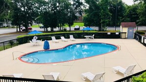A swimming pool with lounge chairs and umbrellas, surrounded by a fence and trees. - 1 King Bed | Mobility Accessible Tub, Nsmk (Savannah GA)