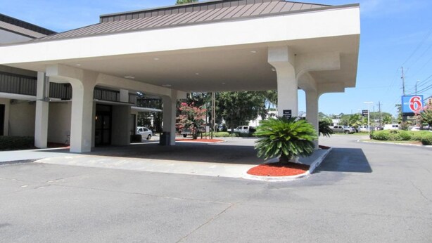 A gas station with a covered parking area, a sign for a Motel 6, and a large green plant in the foreground. - 1 King Bed | Mobility Accessible Tub, Nsmk (Savannah GA)