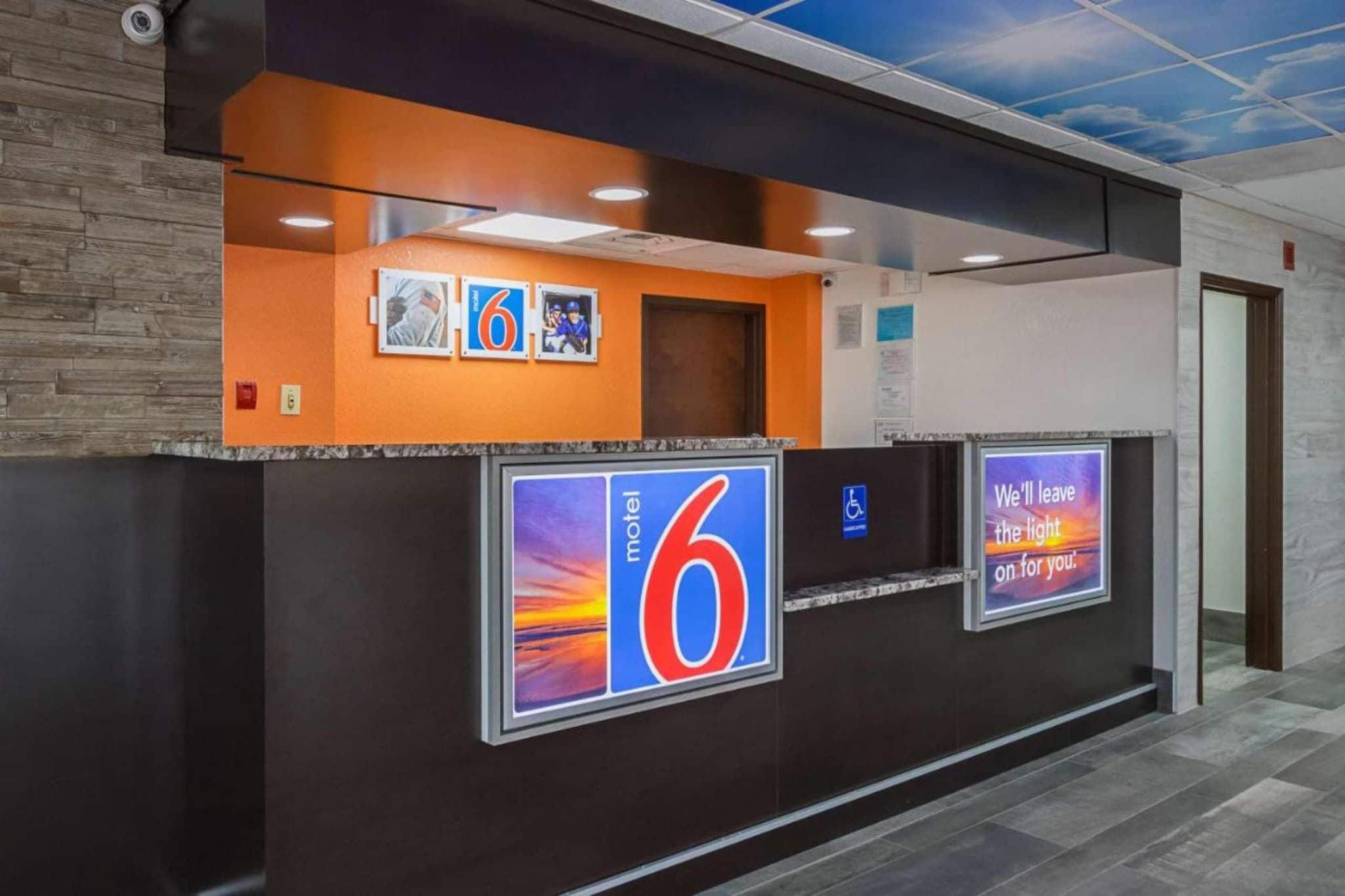 Zona de recepción de un hotel con un llamativo letrero con el número '6', un símbolo de accesibilidad para sillas de ruedas y una pantalla digital mostrando un mensaje.