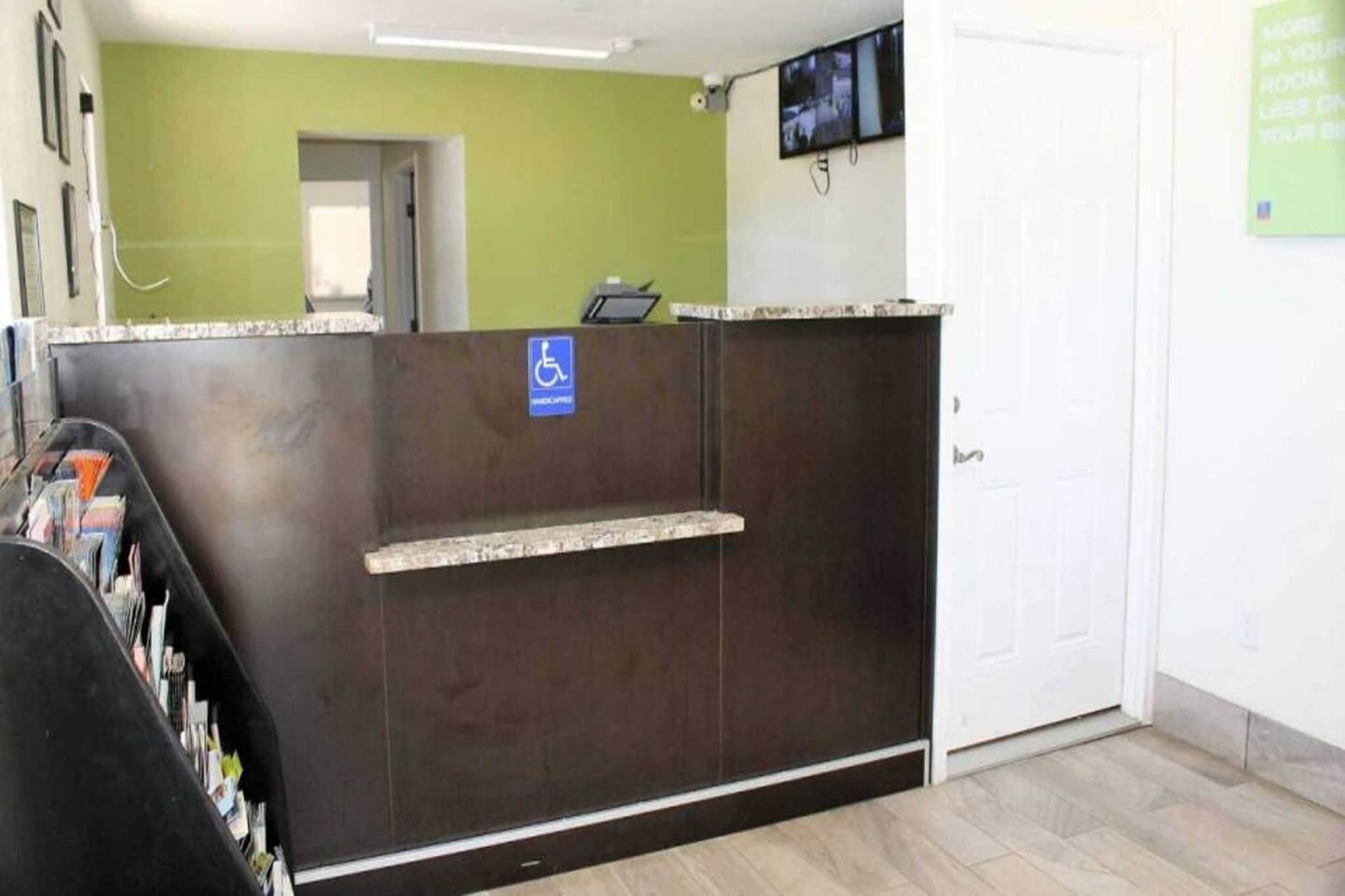 A reception desk with a wheelchair accessibility sign, a television mounted on the wall, and a door to the right.