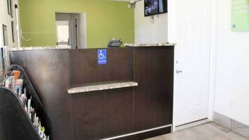 A reception desk with a wheelchair accessibility sign, a television mounted on the wall, and a door to the right.