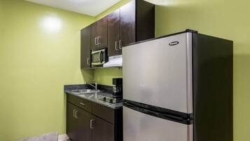 Una cocina compacta con nevera de acero inoxidable, microondas y cafetera sobre la encimera.