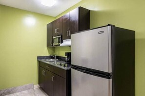 Una cocina compacta con nevera de acero inoxidable, microondas y cafetera sobre la encimera.