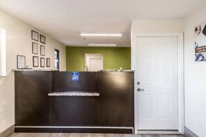 Un área de recepción con mostrador, señal de accesibilidad para sillas de ruedas, certificados enmarcados en la pared, una pared de acento verde y una puerta blanca.