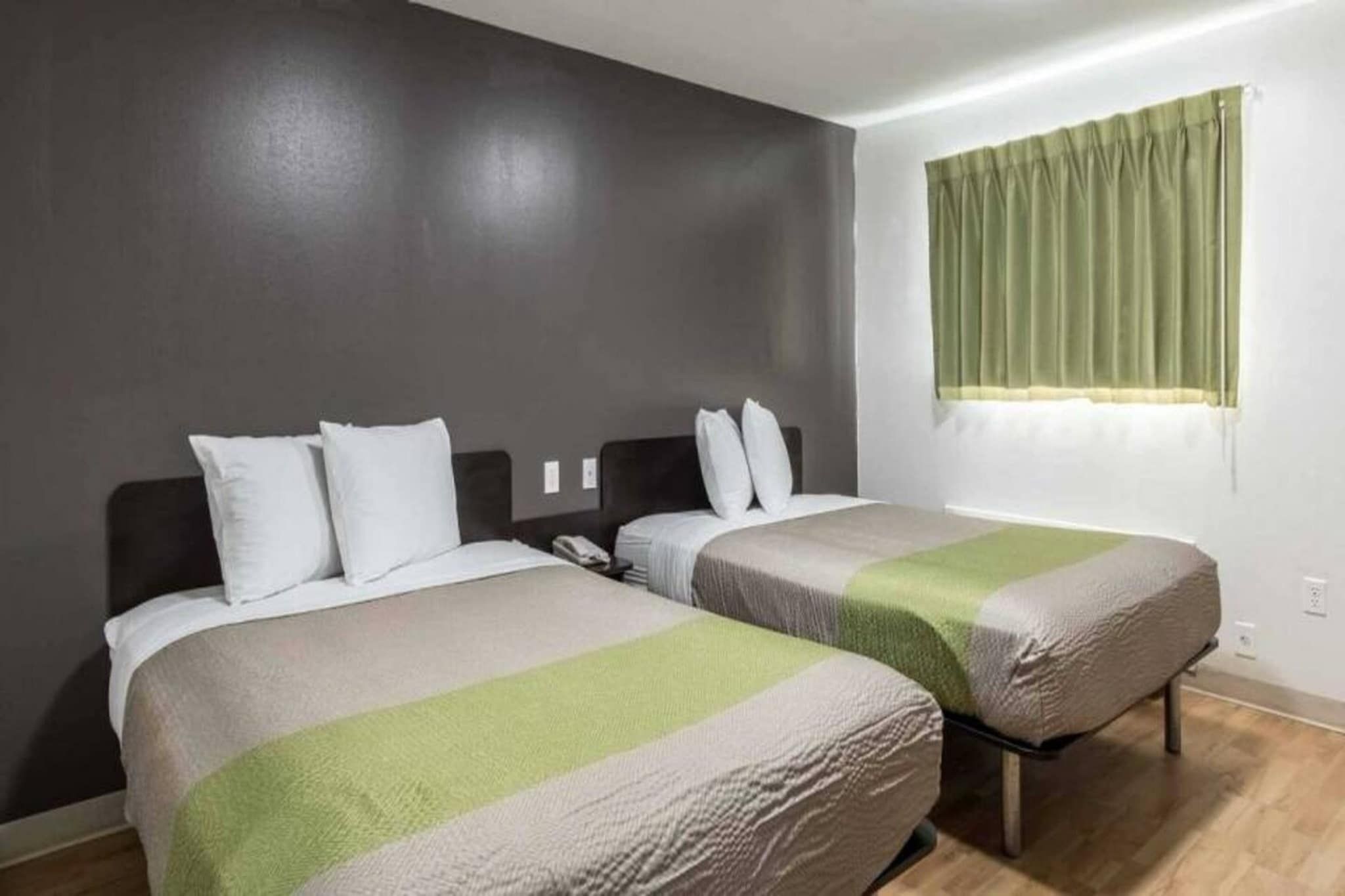 Una habitación de hotel con dos camas, una cortina verde y un teléfono en la mesita de noche.