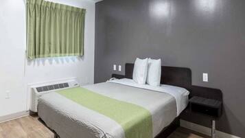 A bedroom with a bed, a bedside table, a wall-mounted heater, and a window with curtains.
